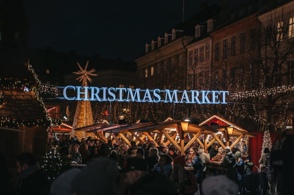 Crowd enjoying Copenhagen Christmas market at night with festive lights and cozy wooden stalls